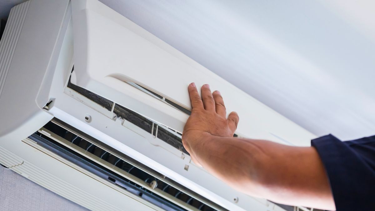 Hand opent de kap van een witte airco binnenunit voor controle en onderhoud van filters en onderdelen van het aircotoestel.
