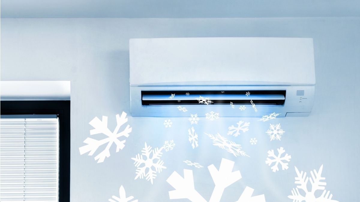 Een witte airco verspreidt koude lucht met sneeuwvlokjes door een witte ruimte. Rechts van de airco zit een raam met zwarte kozijnen en witte lamellen.