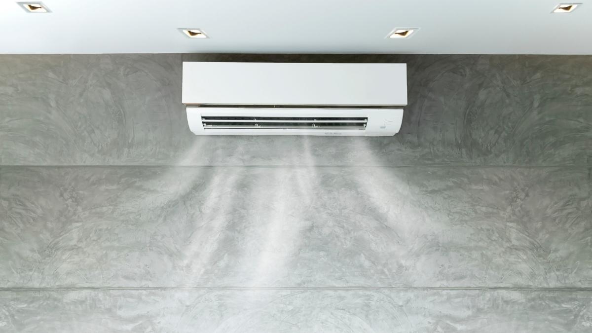 Een witte airco binnenunit onder een wit plafond, tegen een grijze marmeren wand. De airco blaast frisse lucht uit.