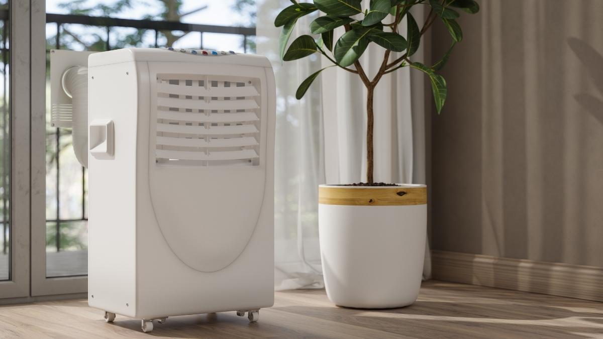 Een witte mobiele airco voor een raam, naast een kamerplant. De afvoerslang loopt via een speciale, vaste afdichting door het raam naar buiten.