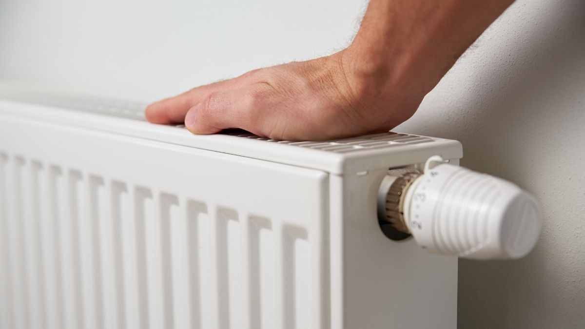 Een hand steunt op een witte radiator tegen een witte muur.