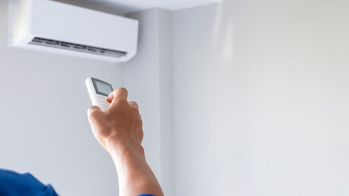 Close-up van een hand die een afstandsbediening gebruikt om een vaste airco-unit te bedienen en de temperatuur te regelen.