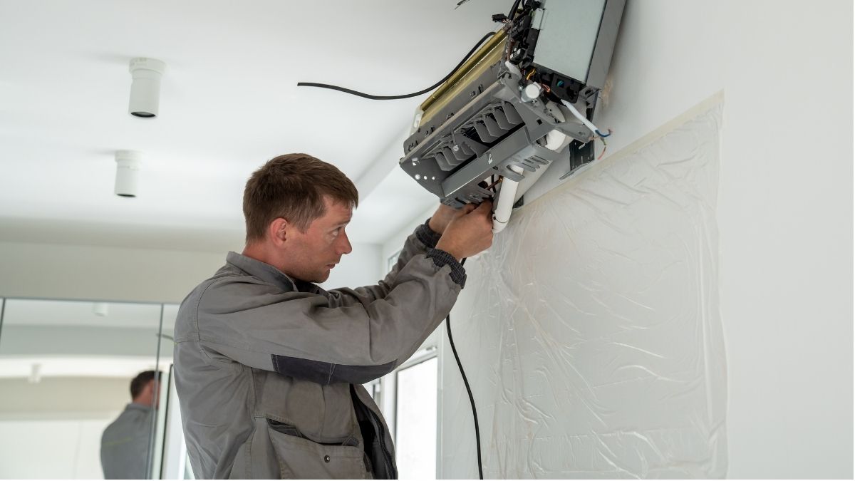 Een airco-installateur in grijze werkkledij is bezig met het monteren van een binnenunit van een mutli-split-airco.