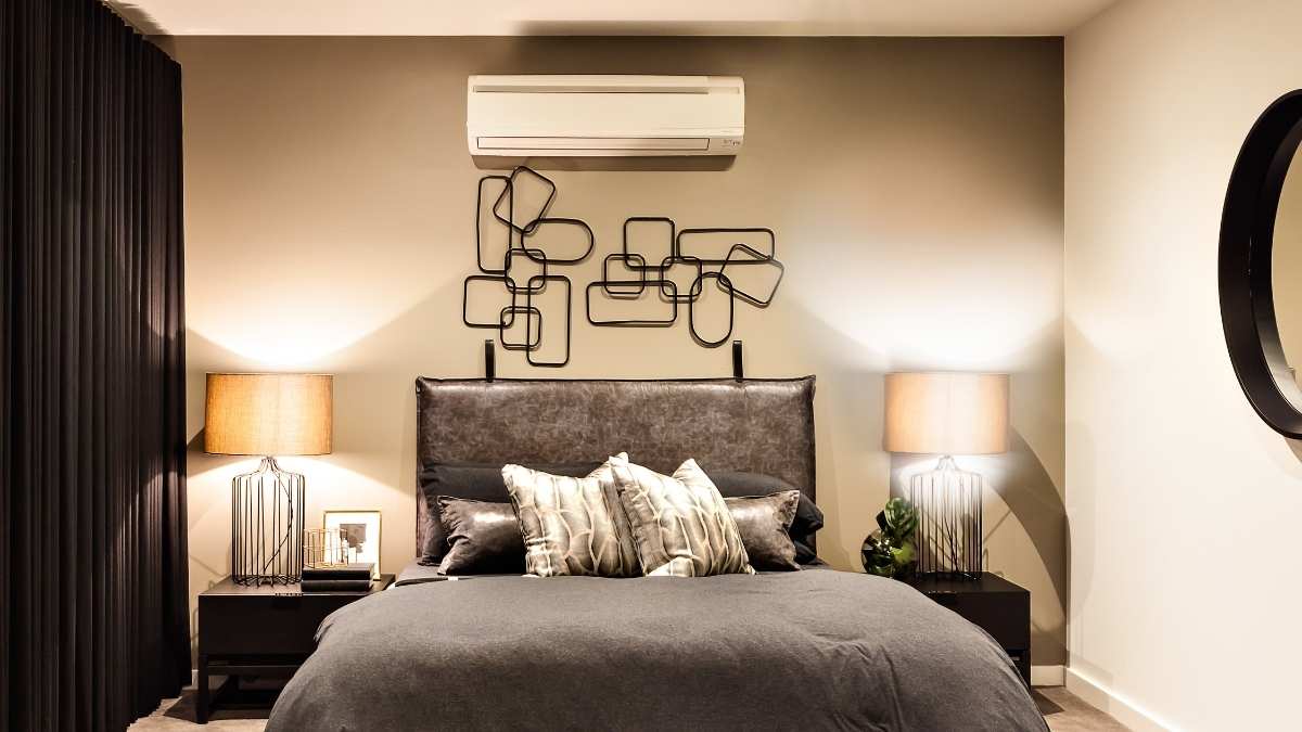 Een luxueuze slaapkamer met airconditioner. De airco hangt boven het bed met grijze lakens en glanzende satijnen kussens.