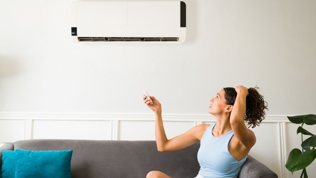Een vrouw met blauw topje zet de airco op in haar woonkamer. Ze houdt haar haren uit haar gezicht met haar vrije hand.