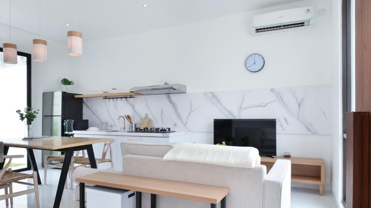 Een woonkamer met open keuken. In de hoek van de kamer hangt een witte binnenunit van een airco.